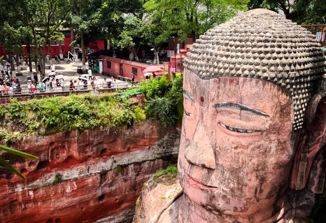 Leshan Giant Buddha with tourists in Chengdu, surrounded by greenery and red cliffs.