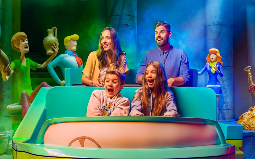 Visitors on a ride at Warner Bros. theme park, Yas Island, Abu Dhabi, surrounded by cartoon characters.