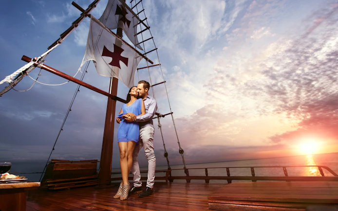 Couple embracing on a sunset cruise in Cancun with Columbus ship sails in the background.