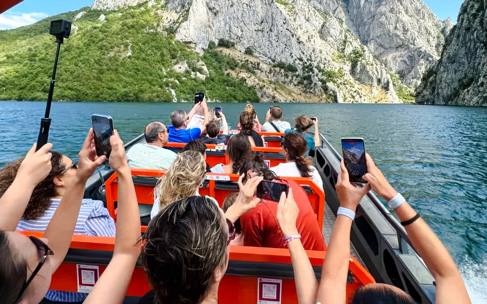 Guests taking photos on a boat tour at Komani Lake and Shala River, surrounded by mountains.