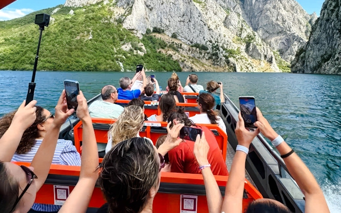 Guests taking photos on a boat tour at Komani Lake and Shala River, surrounded by mountains.