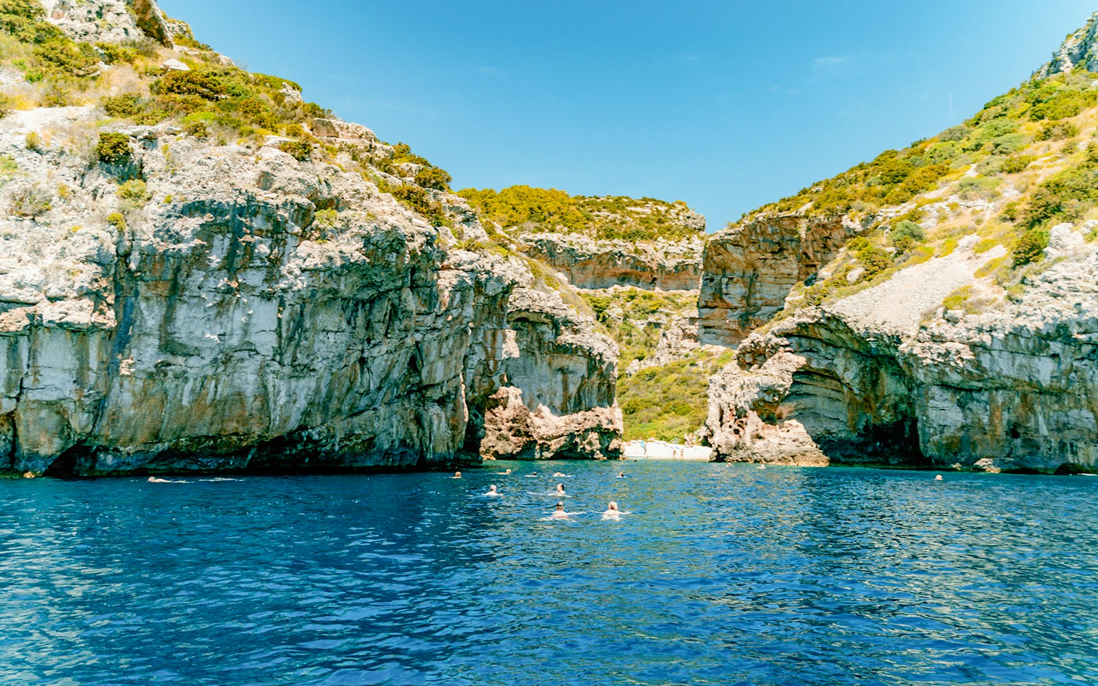 Stiniva Bay view with swimmers in clear blue water surrounded by rocky cliffs, Vis Island, Croatia.