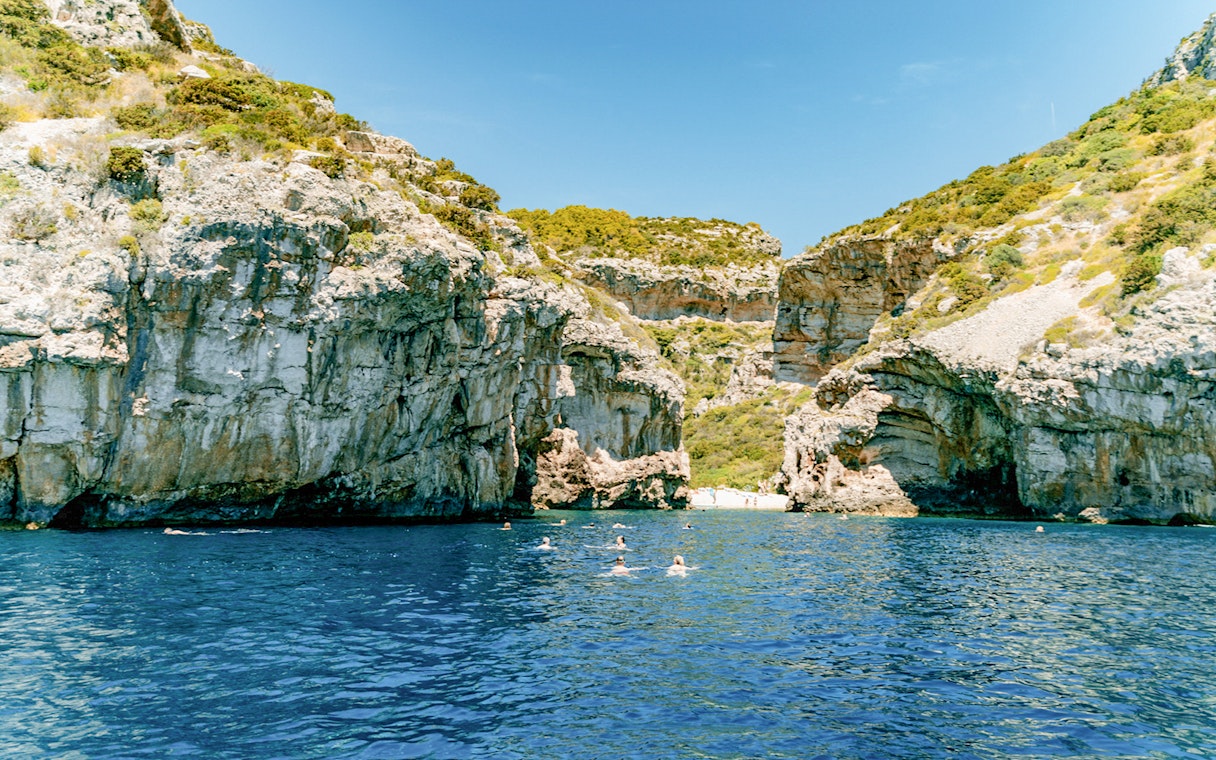 Stiniva Bay view with swimmers in clear blue water surrounded by rocky cliffs, Vis Island, Croatia.