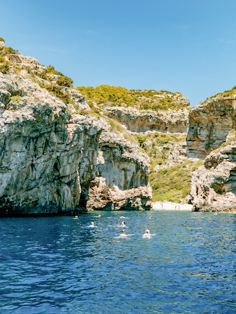 Stiniva Bay view with swimmers in clear blue water surrounded by rocky cliffs, Vis Island, Croatia.