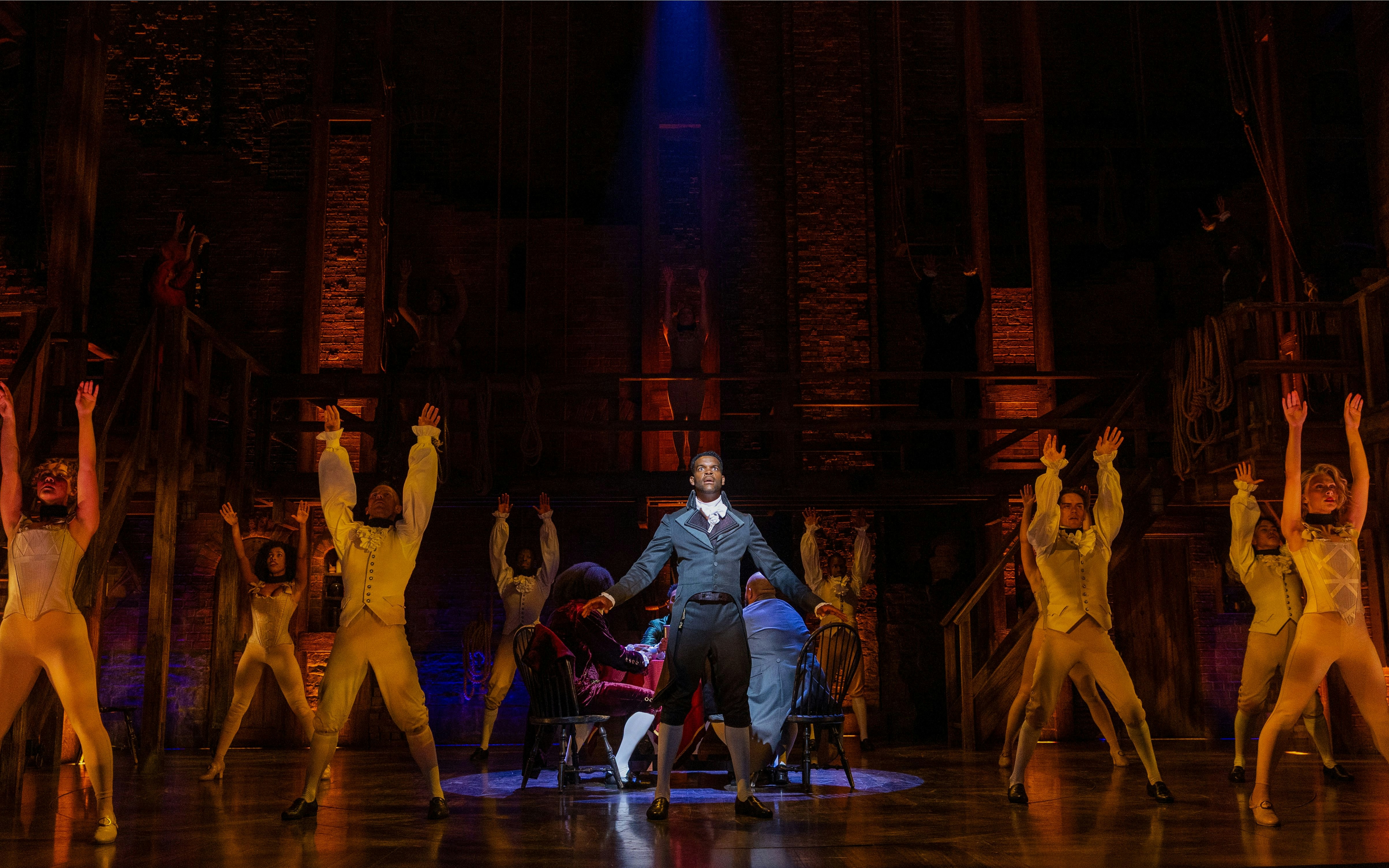 Cast performing a scene from Hamilton on stage with dramatic lighting.