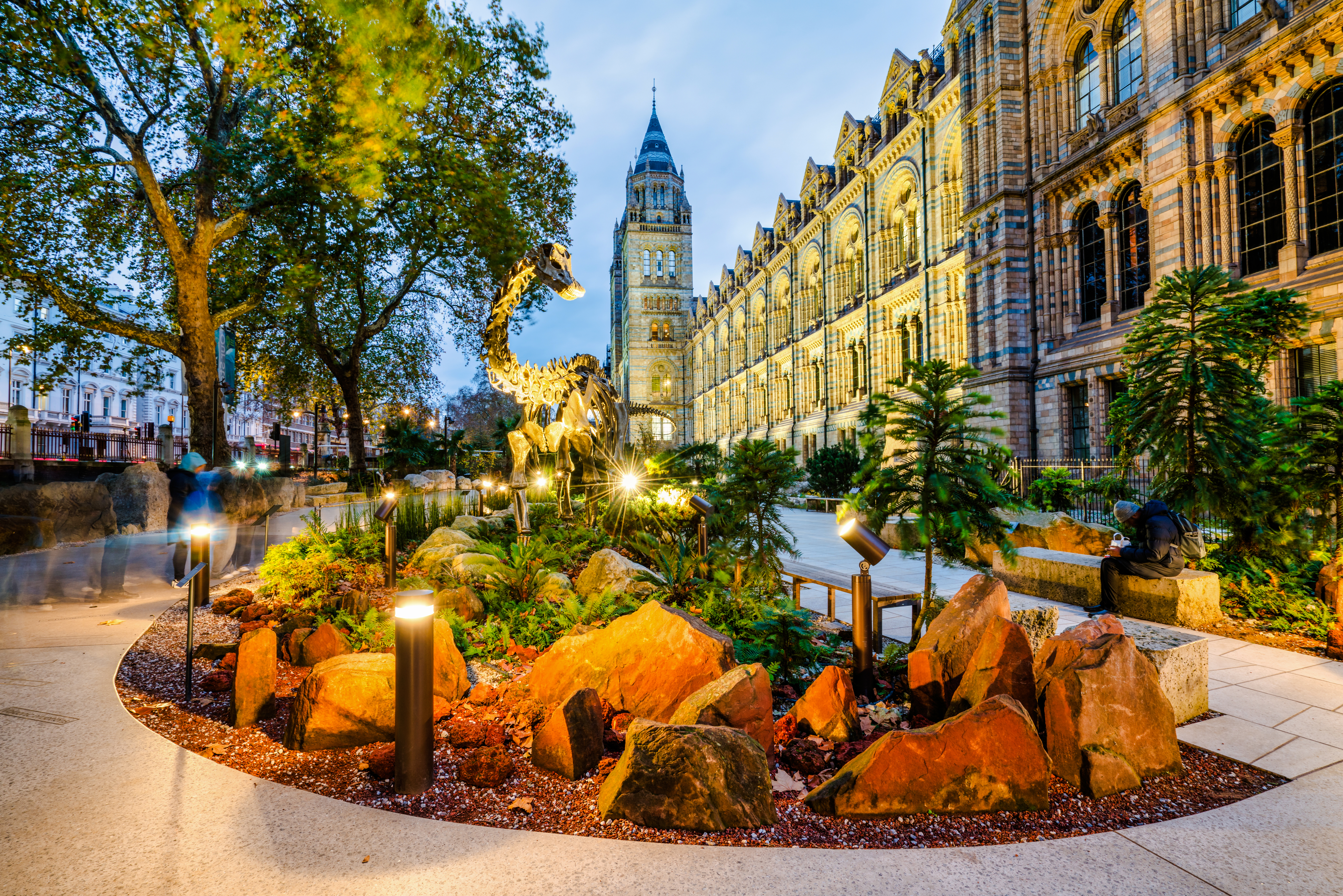 Dinosaur sculpture outside Natural History Museum, London, England, with illuminated facade.