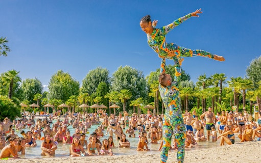 Acrobats performing at a dance show by a pool with a crowd watching.