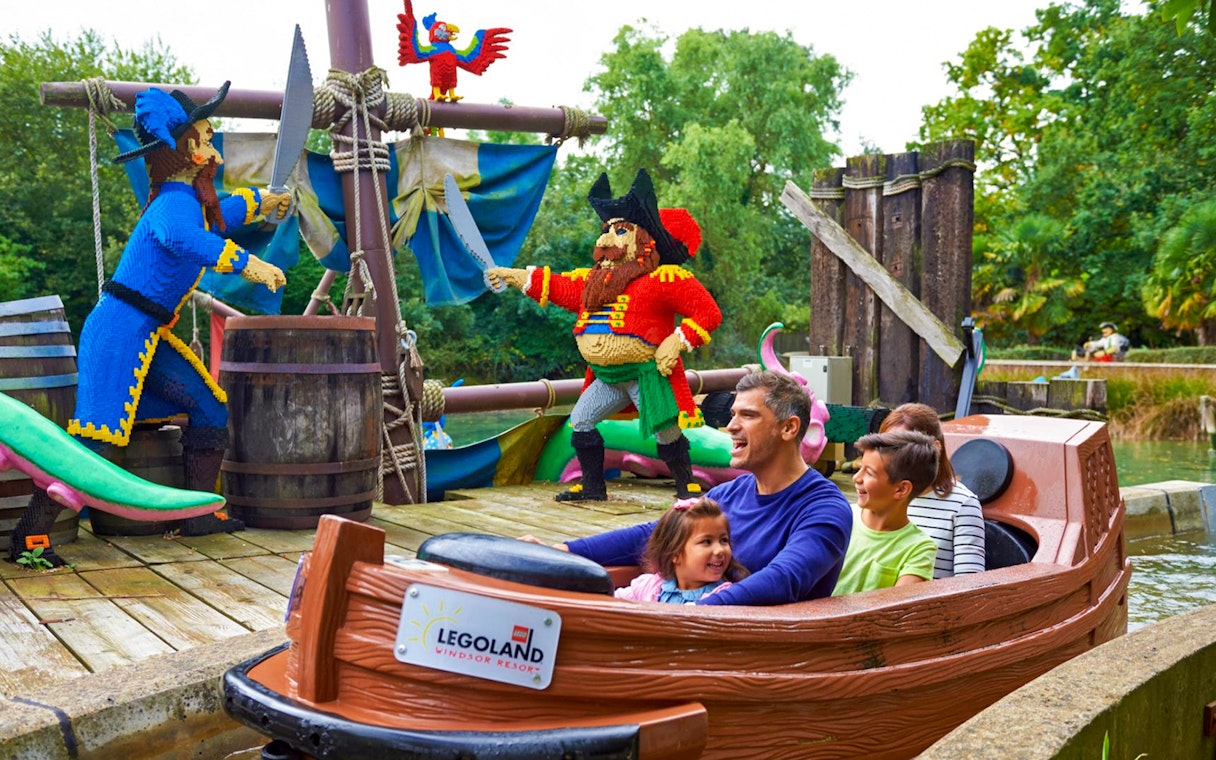 Family enjoying a boat ride past LEGO pirate figures at LEGOLAND Windsor Resort.