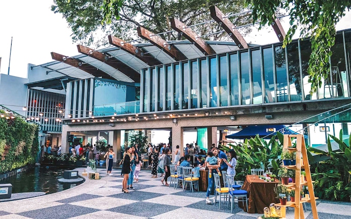 Outdoor gathering at a modern venue in Singapore with people socializing near greenery.
