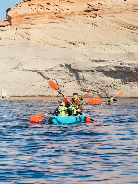 Kayakers paddling on Lake Powell near Antelope Canyon's sandstone cliffs.