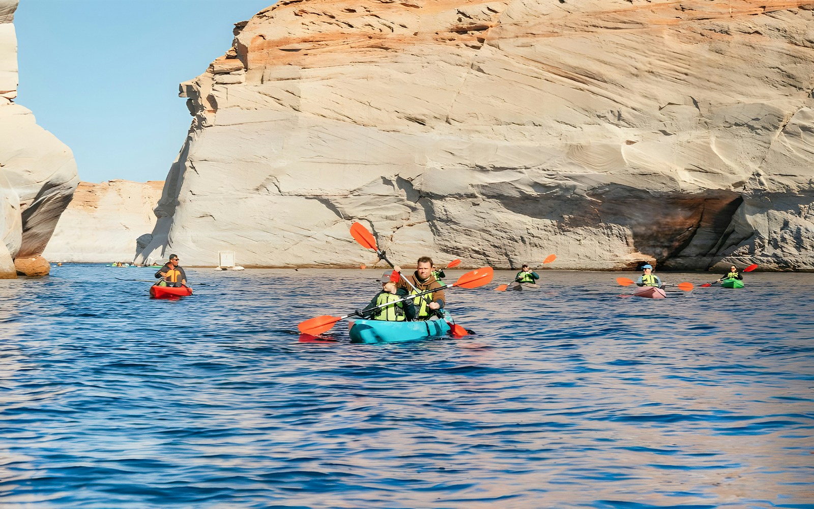 Kayakers paddling on Lake Powell near Antelope Canyon's sandstone cliffs.