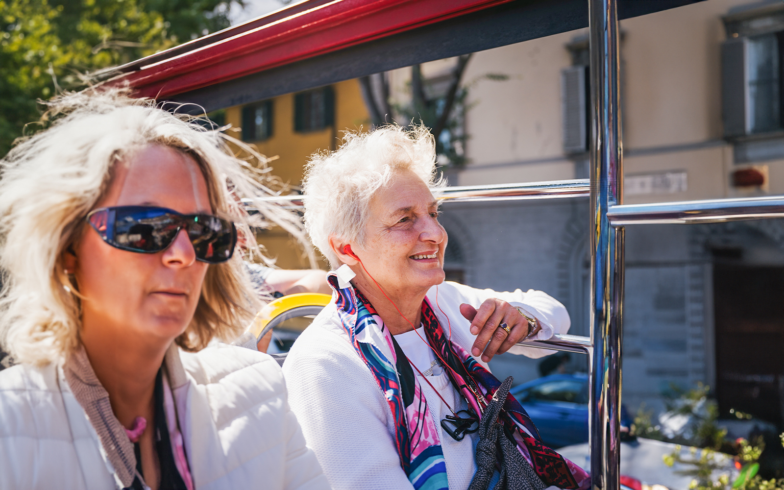 Two elderly women enjoying a city sightseeing tour with audio guides on an open-top bus.