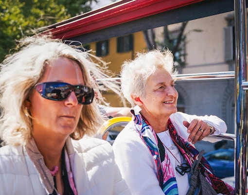 Open-top bus with tourists using city sightseeing audio guide in a European city.