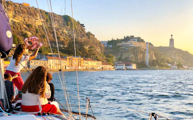 Tourists on a private boat enjoying Lisbon's waterfront view with Cristo Rei statue in the background.