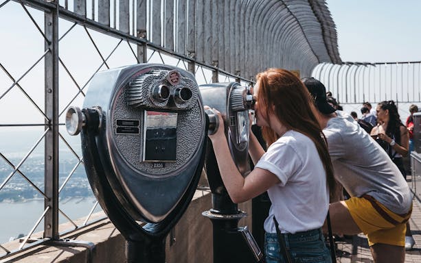 Visitors using binoculars on Empire State Building observation deck, New York City.