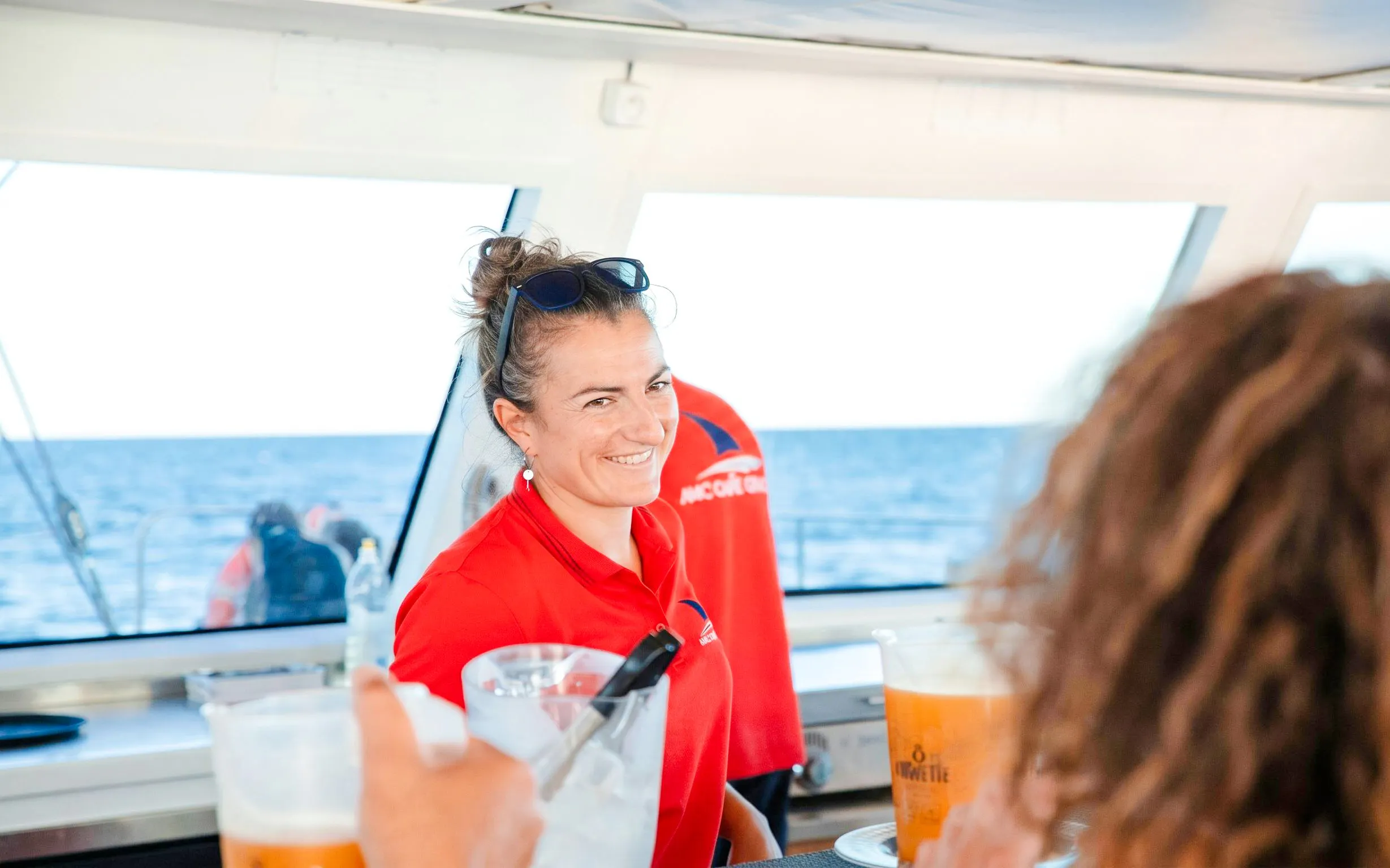 Crew member serving drinks on a catamaran during a sunset cruise.