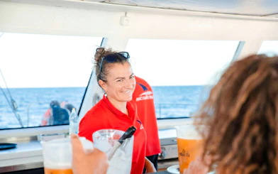 Crew member serving drinks on a catamaran during a sunset cruise.