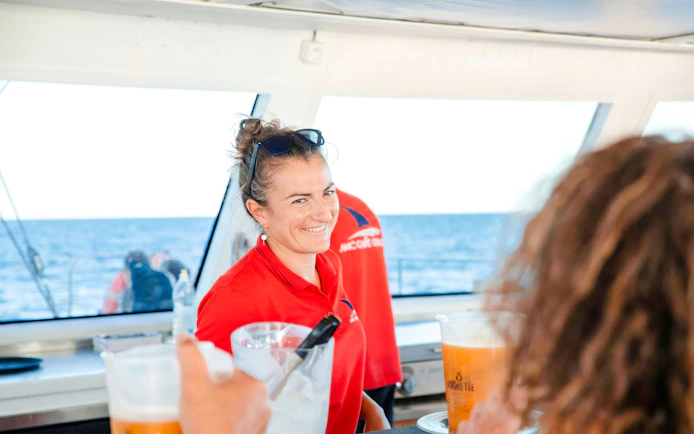 Crew member serving drinks on a catamaran during a sunset cruise.