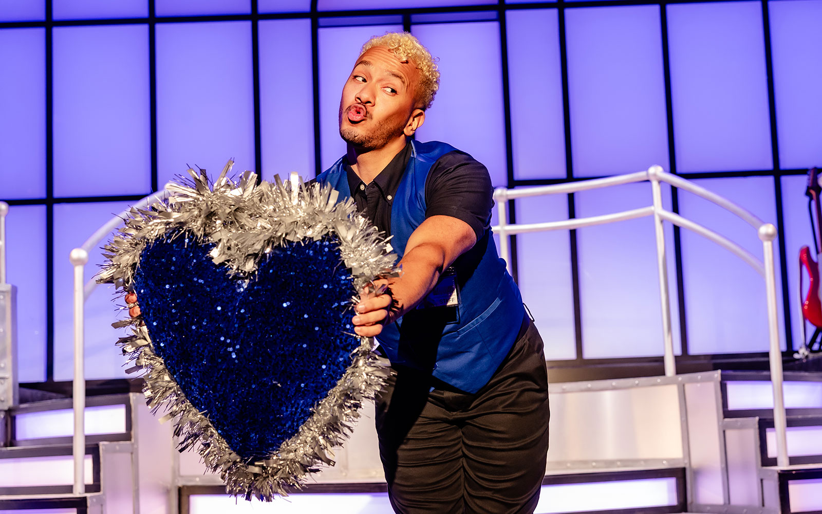Performer holding a glittery heart prop on Titanique West End stage.