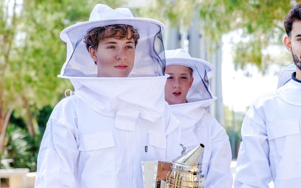 Tourists in beekeeping suits holding a smoker during a beekeeping experience.