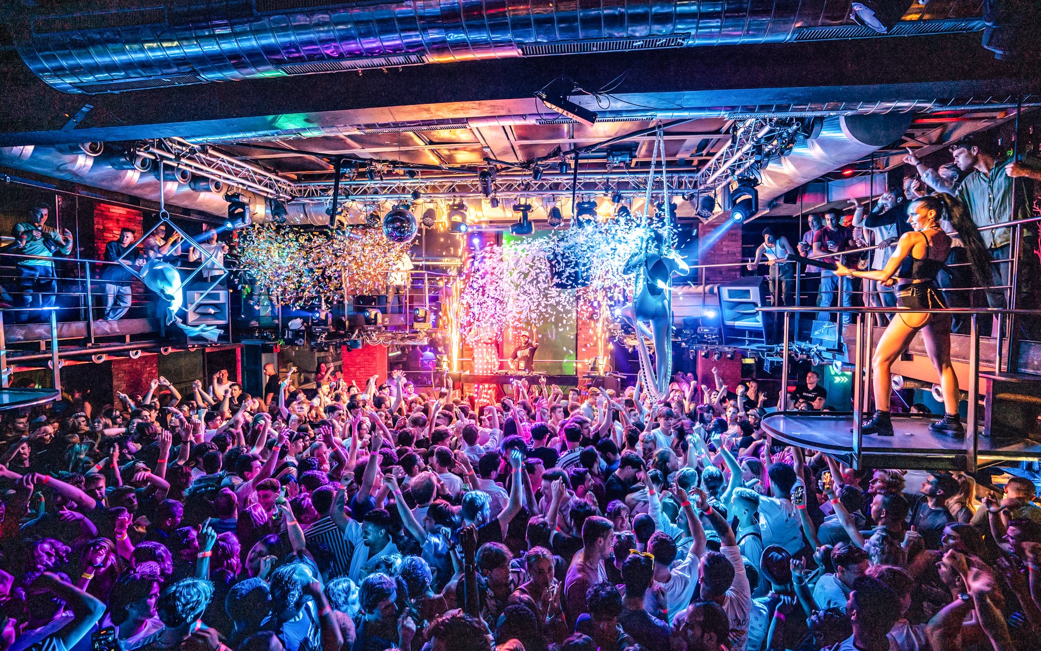 Crowded dance floor at a vibrant sunset boat party in Prague with DJ and confetti.