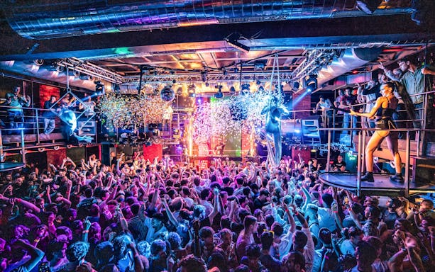 Crowded dance floor at a vibrant sunset boat party in Prague with DJ and confetti.