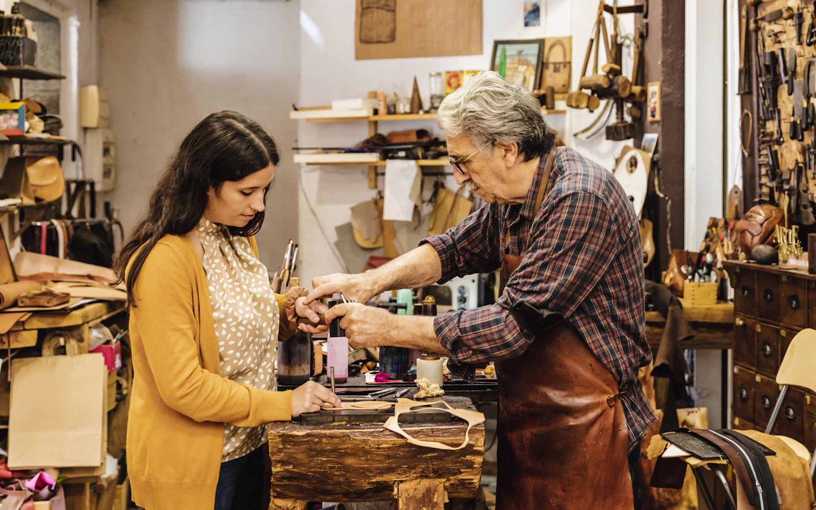 Craftsman demonstrating leatherwork to a tourist at Poble Espanyol workshop.