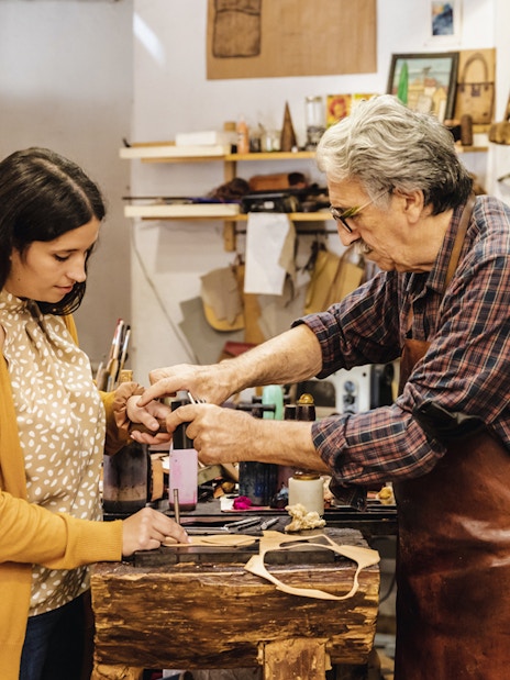 Craftsman demonstrating leatherwork to a tourist at Poble Espanyol workshop.
