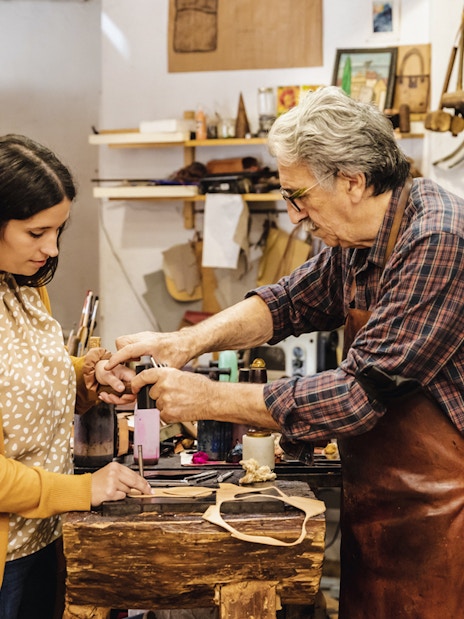 Craftsman demonstrating leatherwork to a tourist at Poble Espanyol workshop.
