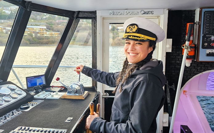 Crew member in captain's hat steering Million Dollar Cruise boat on Lake Wakatipu, Queenstown.
