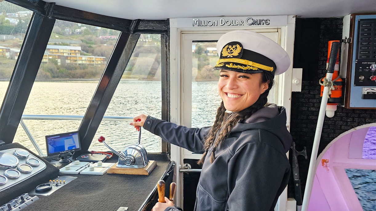 Crew member in captain's hat steering Million Dollar Cruise boat on Lake Wakatipu, Queenstown.