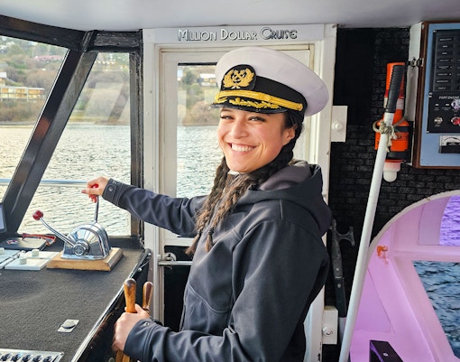 Crew member in captain's hat steering Million Dollar Cruise boat on Lake Wakatipu, Queenstown.