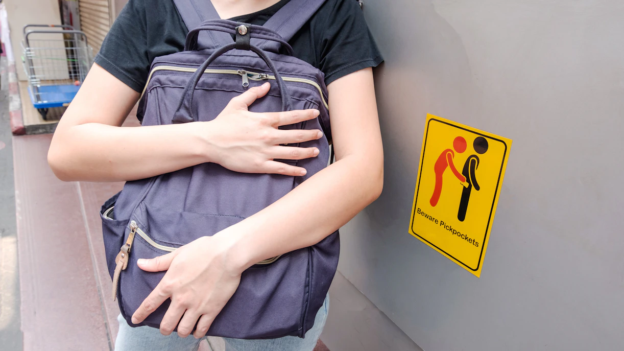 Person holding backpack tightly next to a "Beware Pickpockets" sign in Paris.