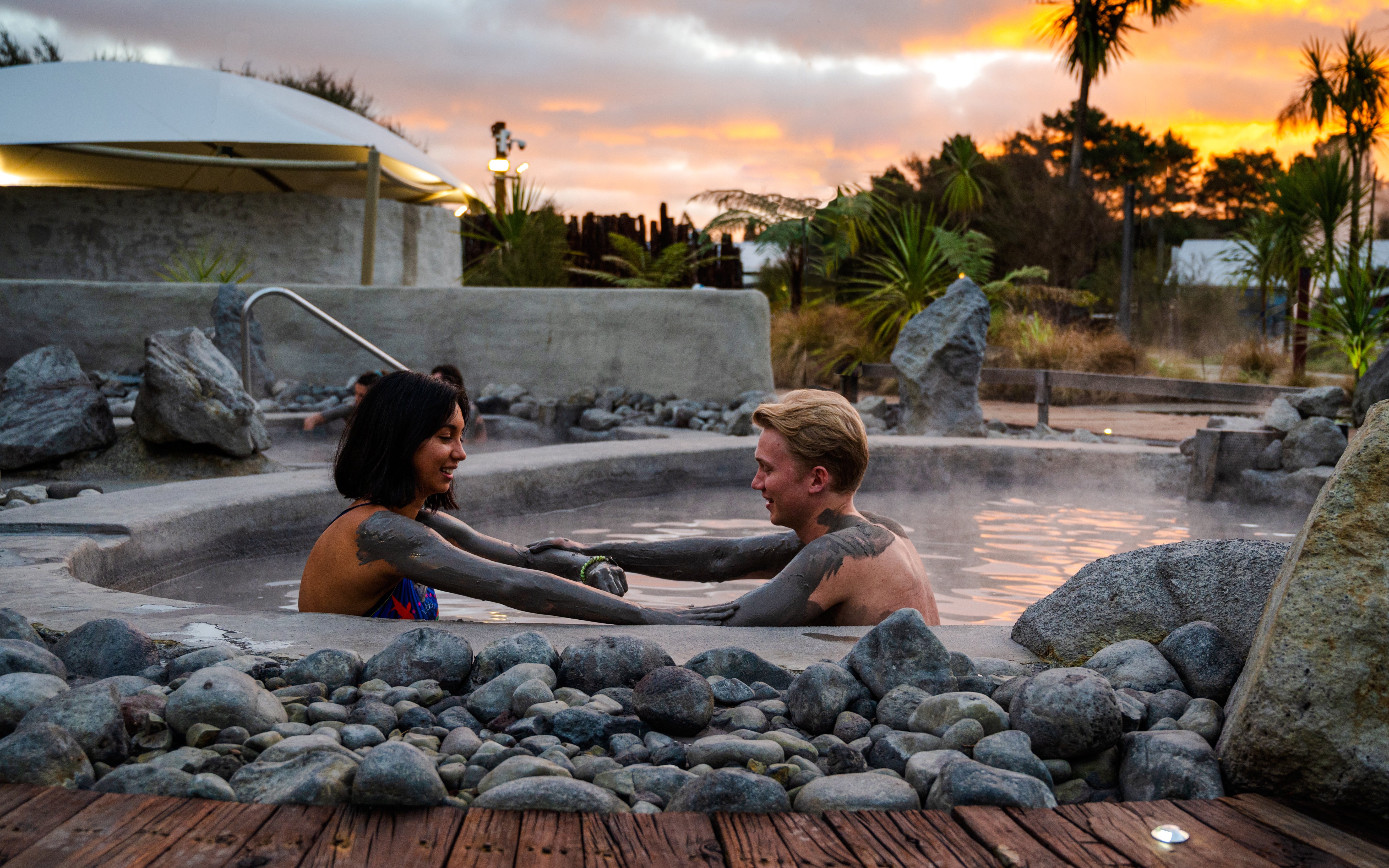 Couple enjoying a mud bath at Hell's Gate geothermal spa at sunset.