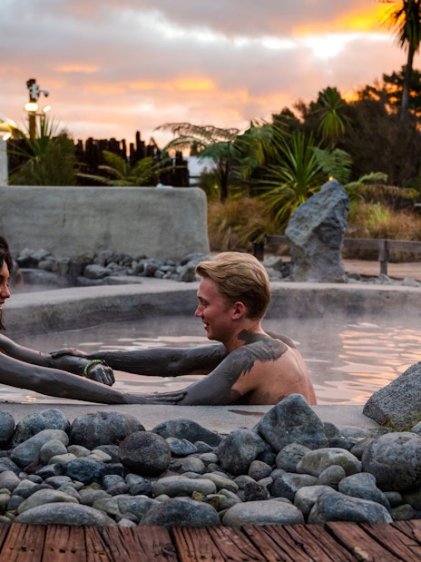 Couple enjoying a mud bath at Hell's Gate geothermal spa at sunset.