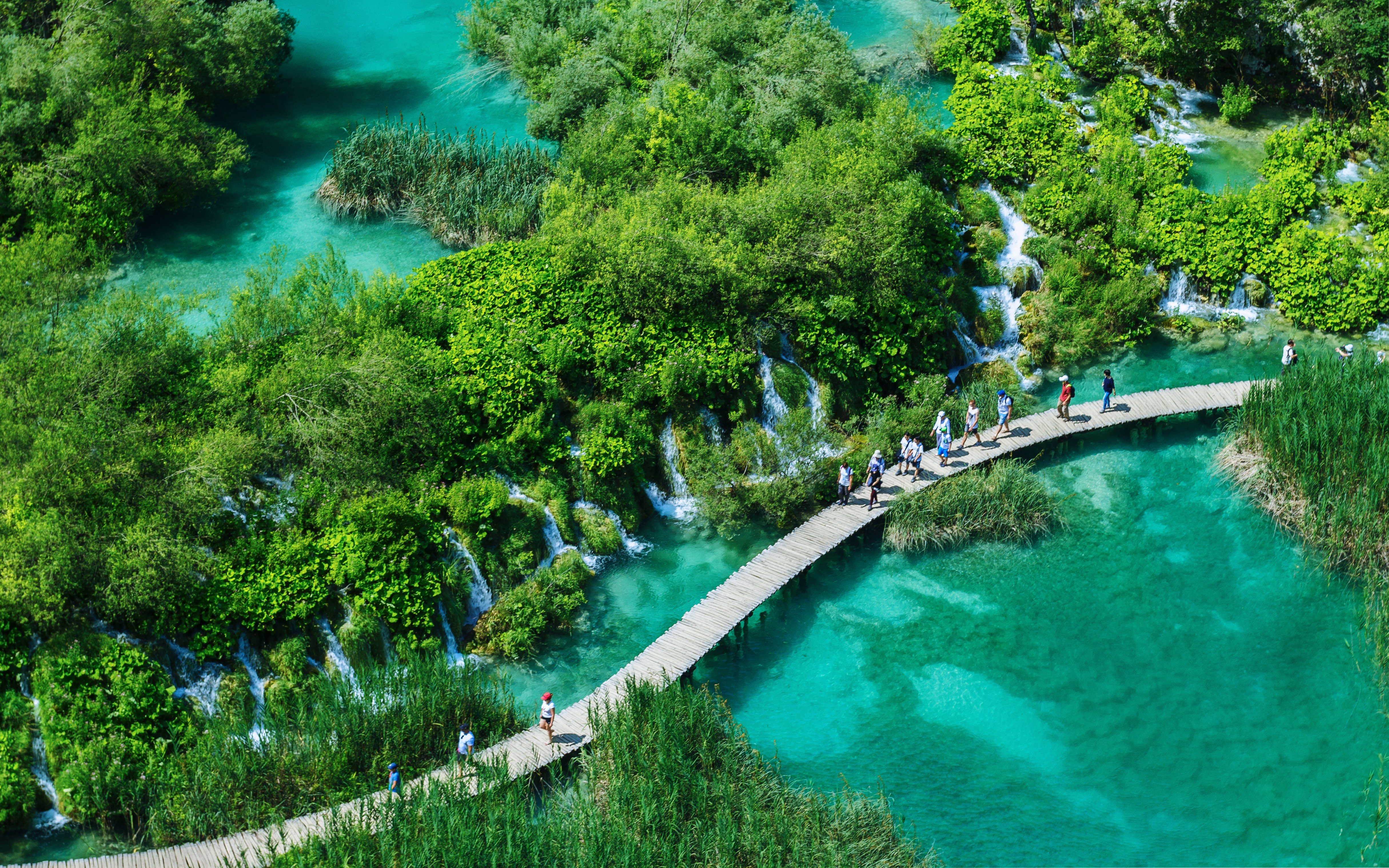 Visitors walking on a wooden path over turquoise lakes in Plitvice Lakes National Park, Croatia.