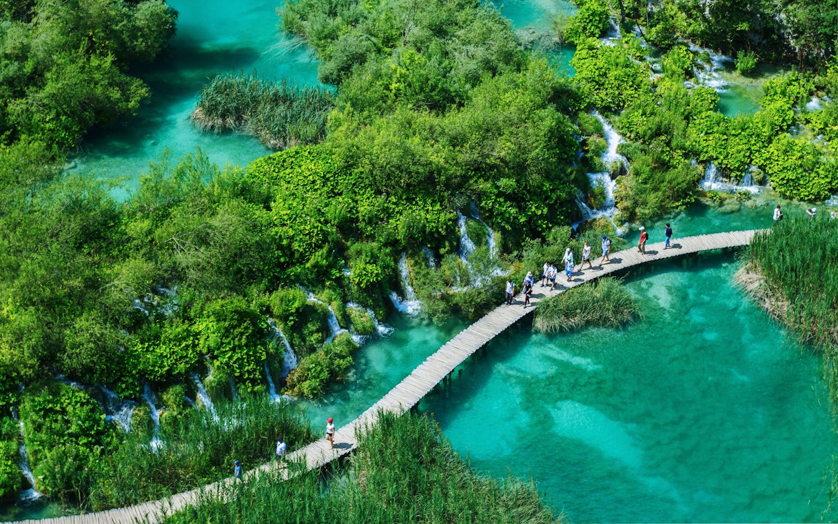 Visitors walking on a wooden path over turquoise lakes in Plitvice Lakes National Park, Croatia.