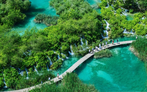 Visitors walking on a wooden path over turquoise lakes in Plitvice Lakes National Park, Croatia.