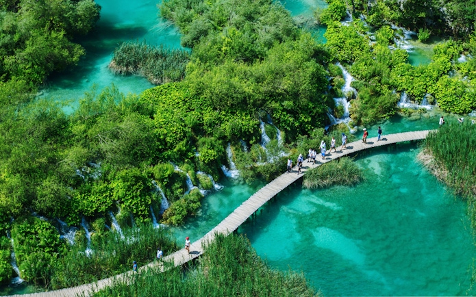 Visitors walking on a wooden path over turquoise lakes in Plitvice Lakes National Park, Croatia.