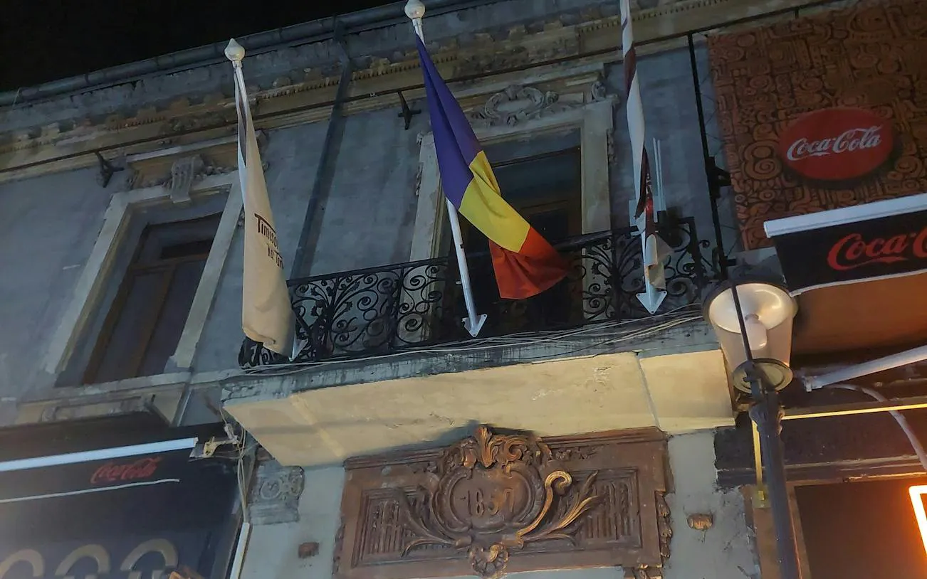 Romanian flag on a historic building facade in Bucharest at night.