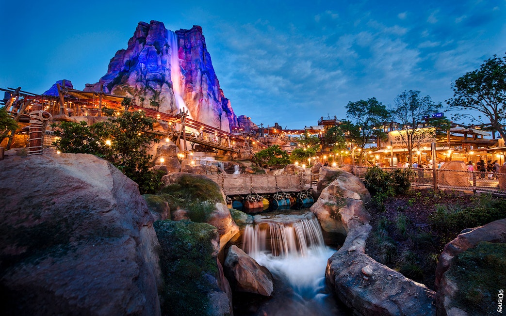 Shanghai Disney Adventure Isle with waterfall and illuminated rock formations at dusk.