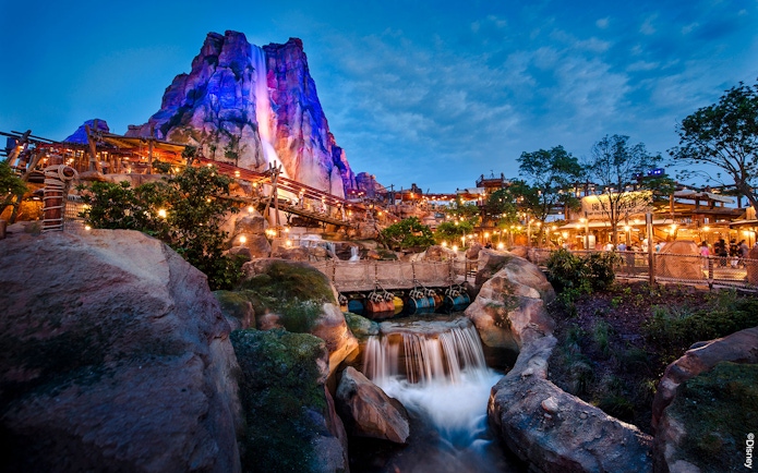 Shanghai Disney Adventure Isle with waterfall and illuminated rock formations at dusk.