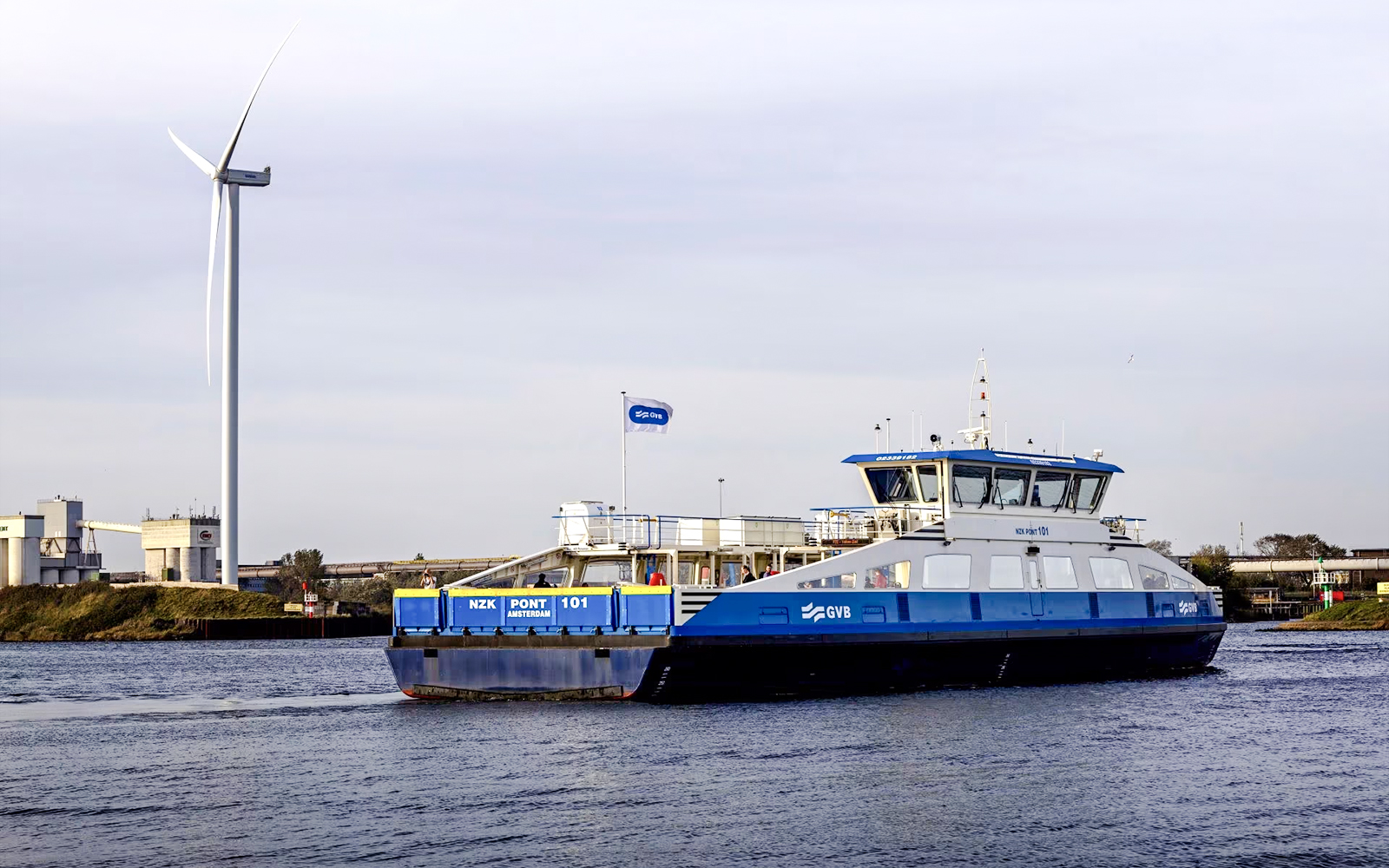 Ferry crossing a canal in Amsterdam with a wind turbine in the background.