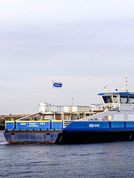 Ferry crossing a canal in Amsterdam with a wind turbine in the background.