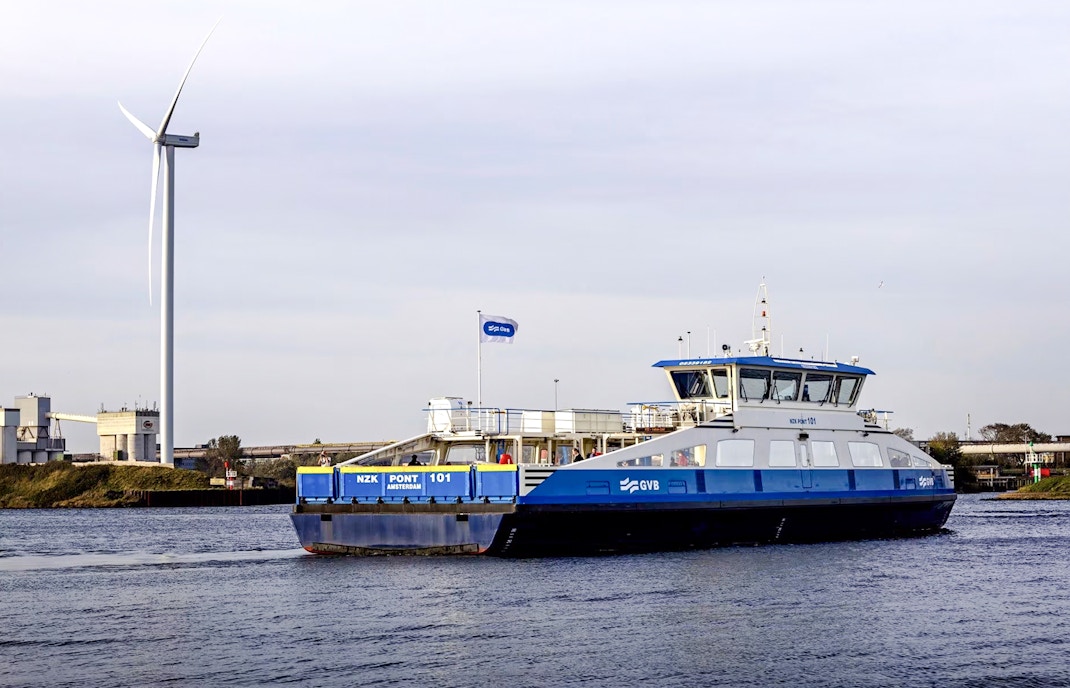 Ferry crossing a canal in Amsterdam with a wind turbine in the background.