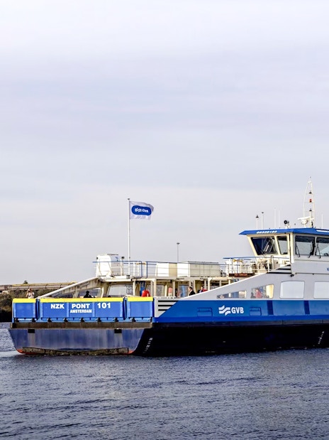 Ferry crossing a canal in Amsterdam with a wind turbine in the background.