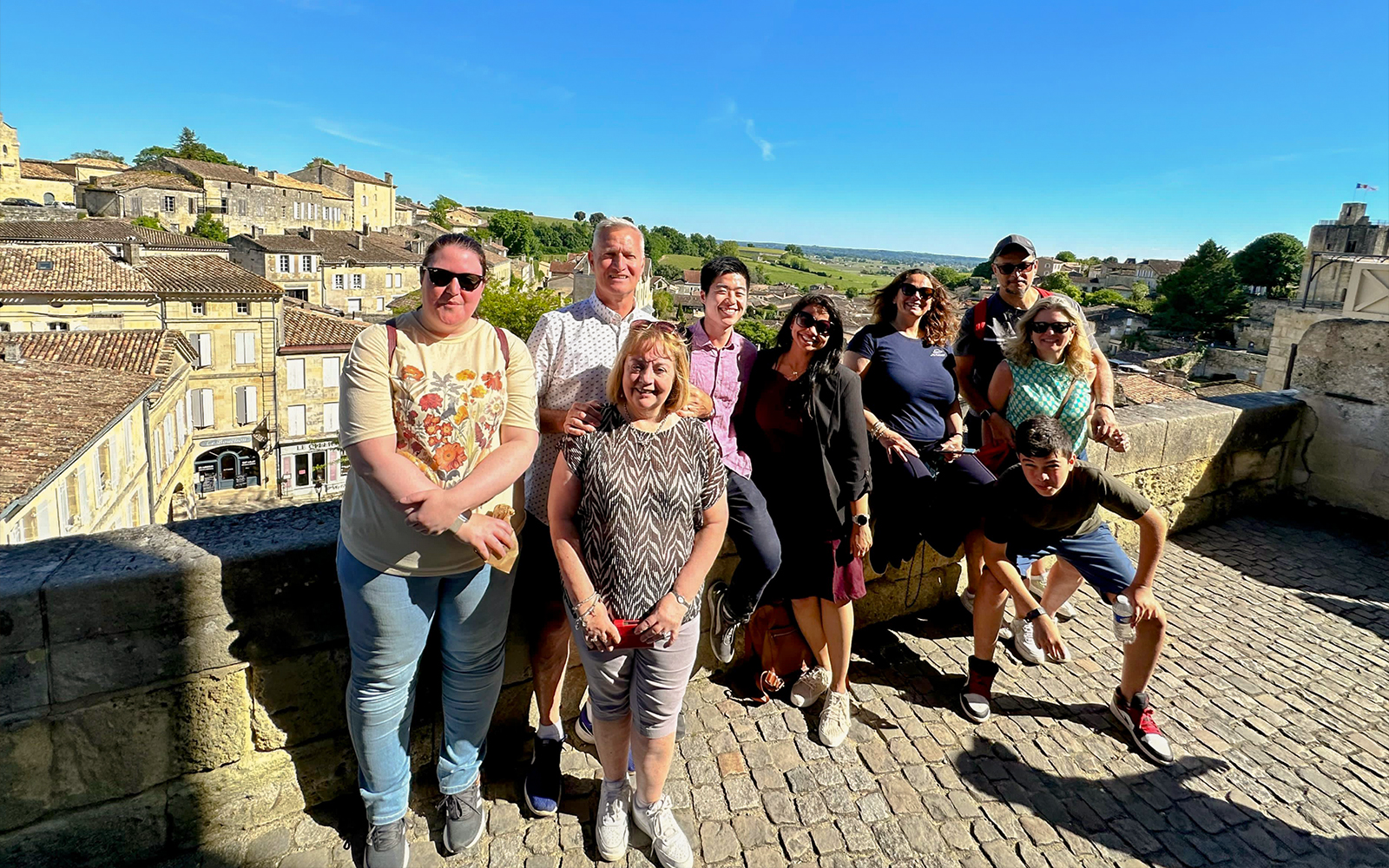 Tour group enjoying a sunny day in Saint-Emilion village with historic buildings in the background.