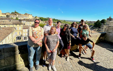 Tour group enjoying a sunny day in Saint-Emilion village with historic buildings in the background.