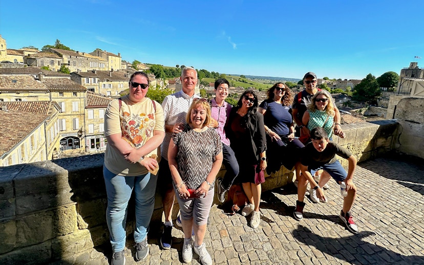 Tour group enjoying a sunny day in Saint-Emilion village with historic buildings in the background.