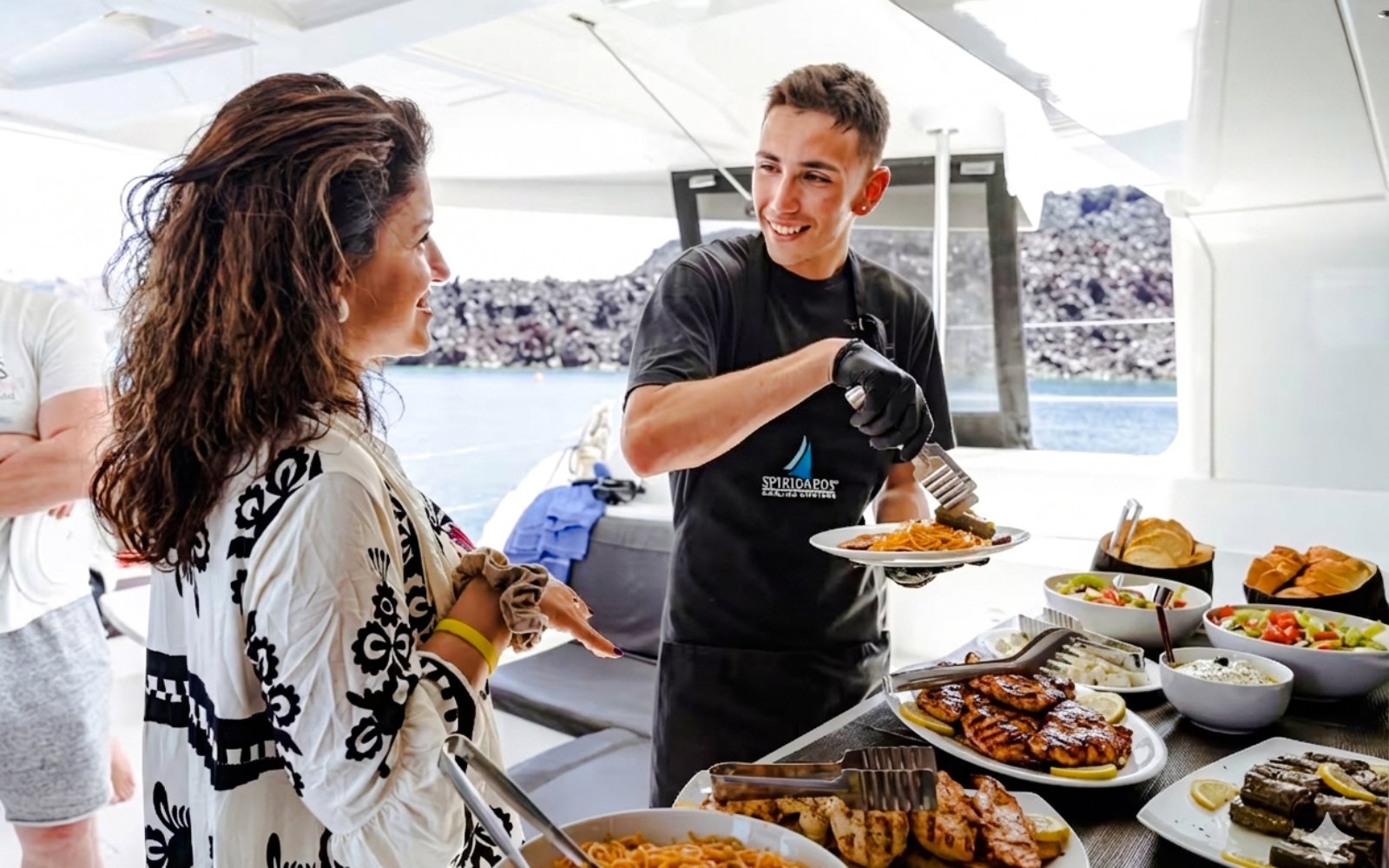 Guests being served food on a catamaran cruise with views of the sea in the background.